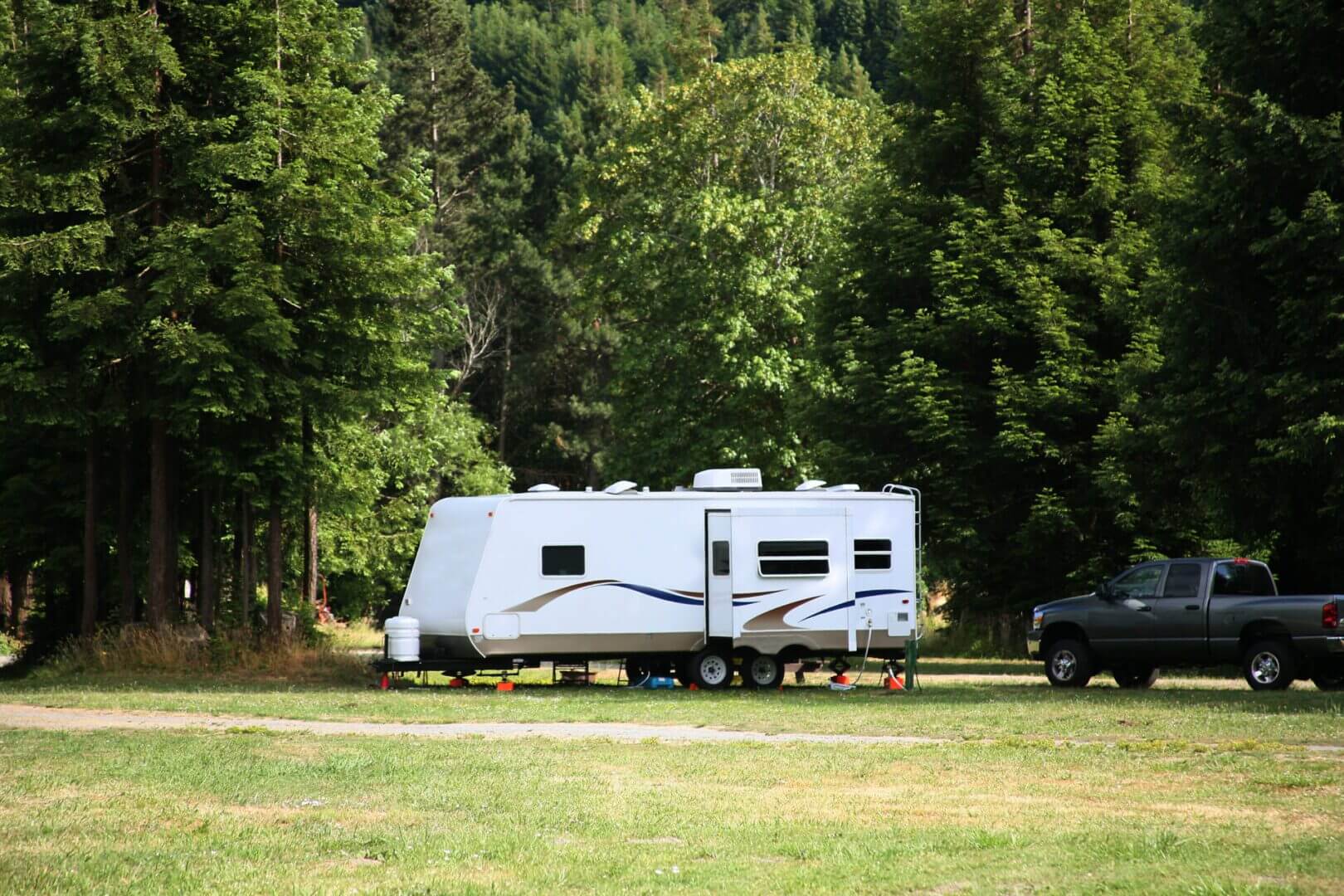 Camper and truck parked in forest clearing.