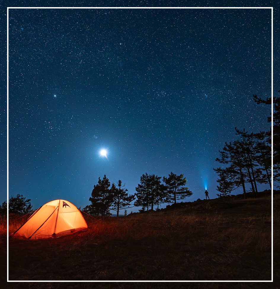 Glowing tent under starry night sky.