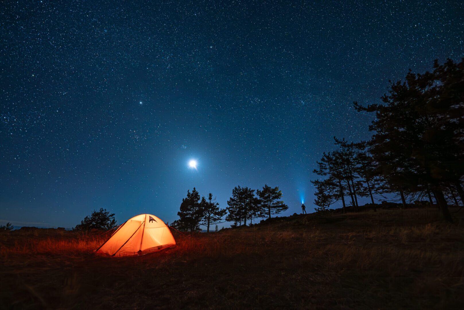 Tent under starry night sky and moon.