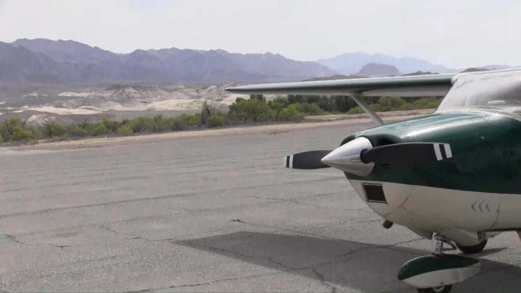 Small airplane parked on a runway with mountains in the background.
