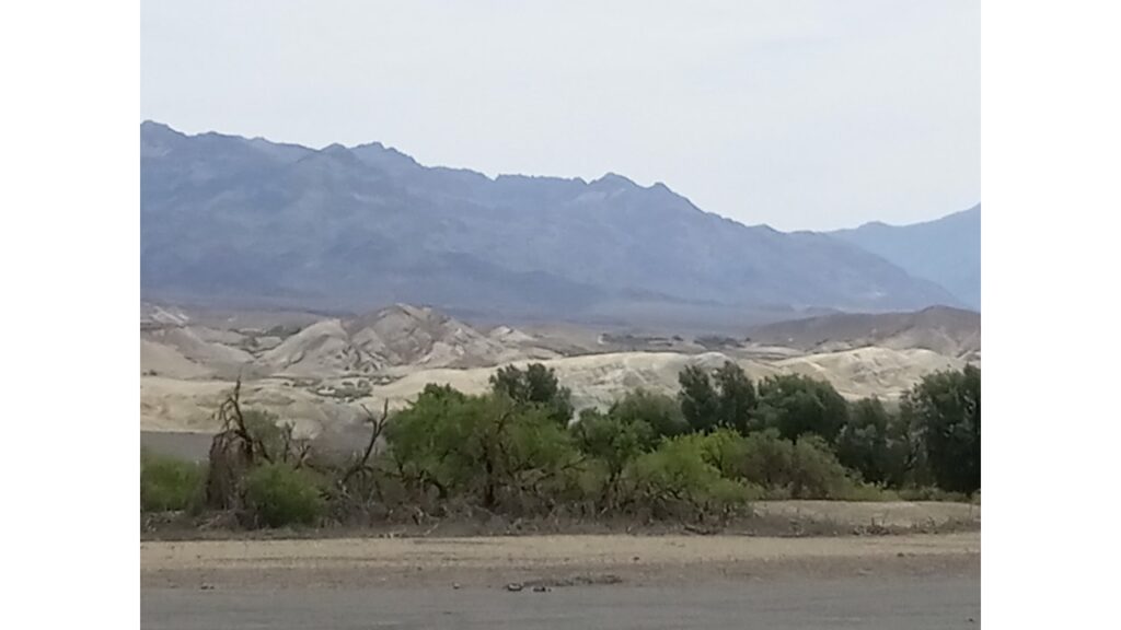 Desert landscape with mountains and sparse greenery under a cloudy sky.