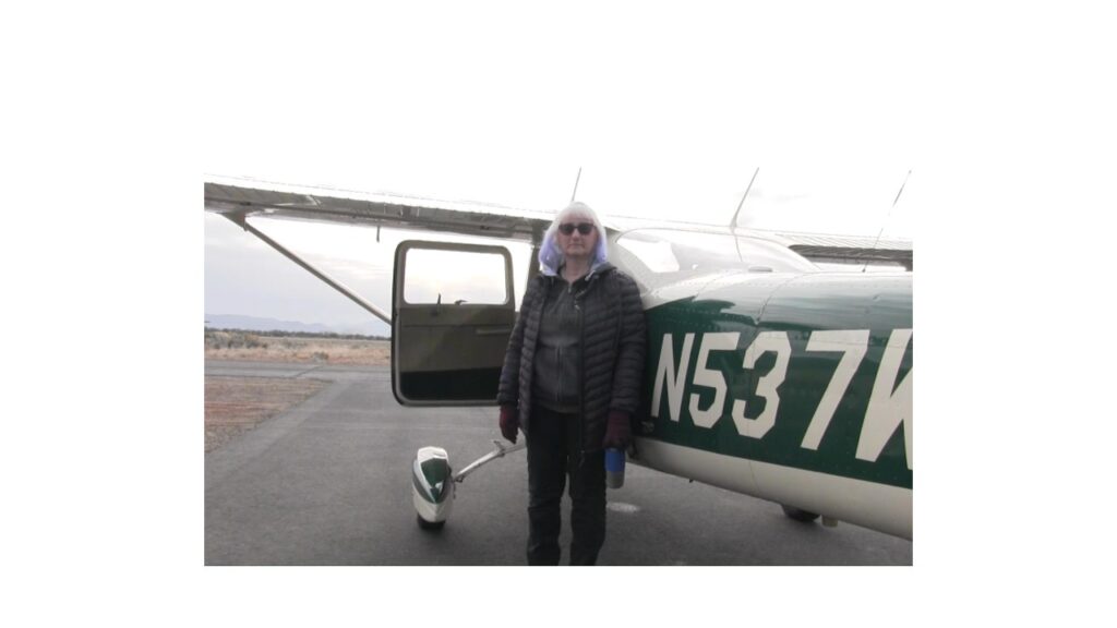 Man standing next to a small private airplane on a cloudy day.